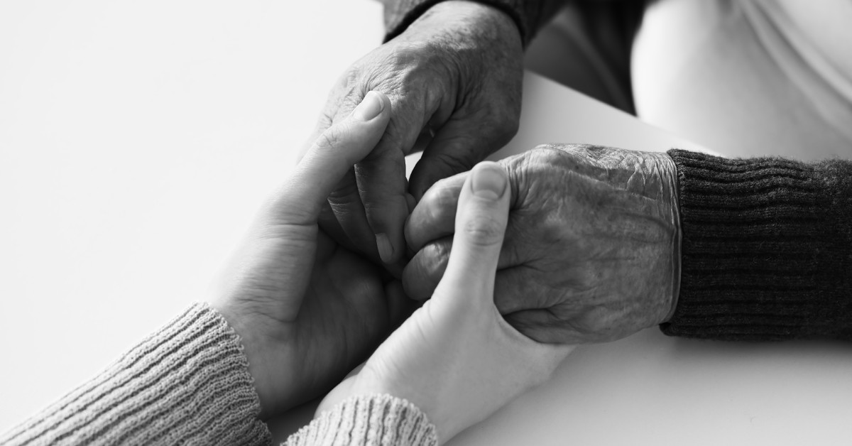 Two sets of hands embracing each other over the tabletop. One pair is older and the other is younger.